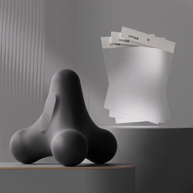 Matte black ergonomic massage tool next to transparent OPP packaging bags in minimalist product display